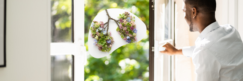 Picture of a man opening a window to an exterior with trees. There is a floral representation of a pair of lungs in an organic shape overlaid on the image.